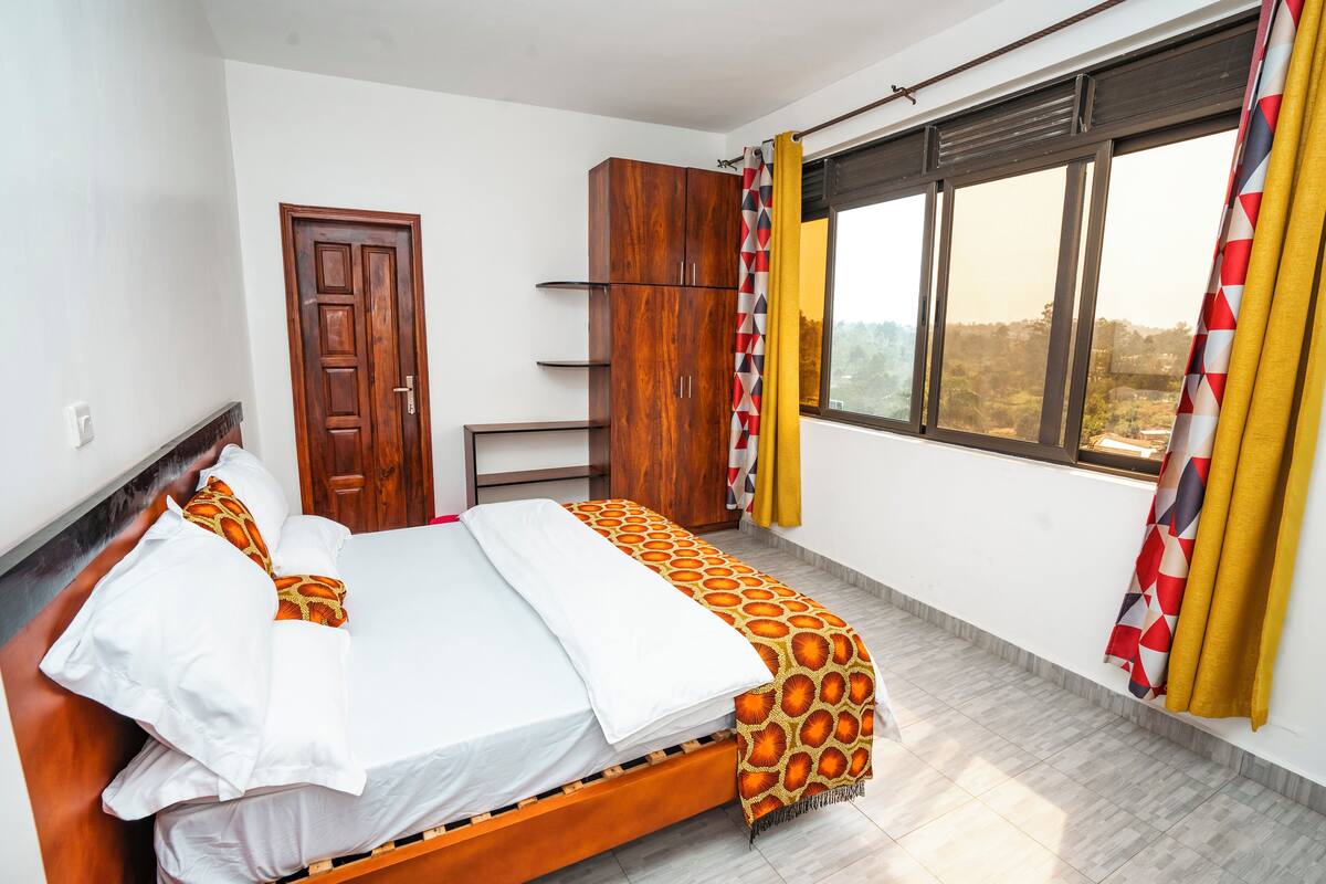 Un dormitorio con una cama de madera, ropa de cama blanca, un armario y una ventana con cortinas.