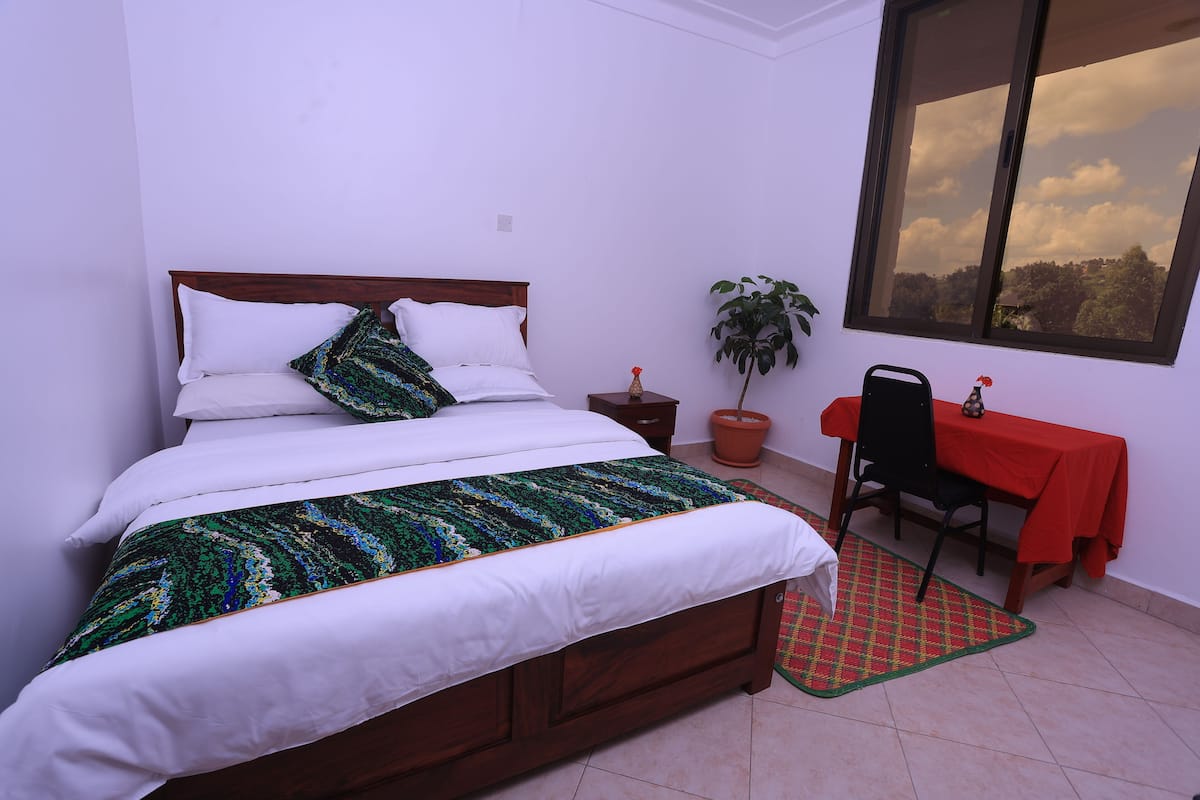 Un dormitorio con cama, planta en maceta, una mesa roja y ventana con vistas.