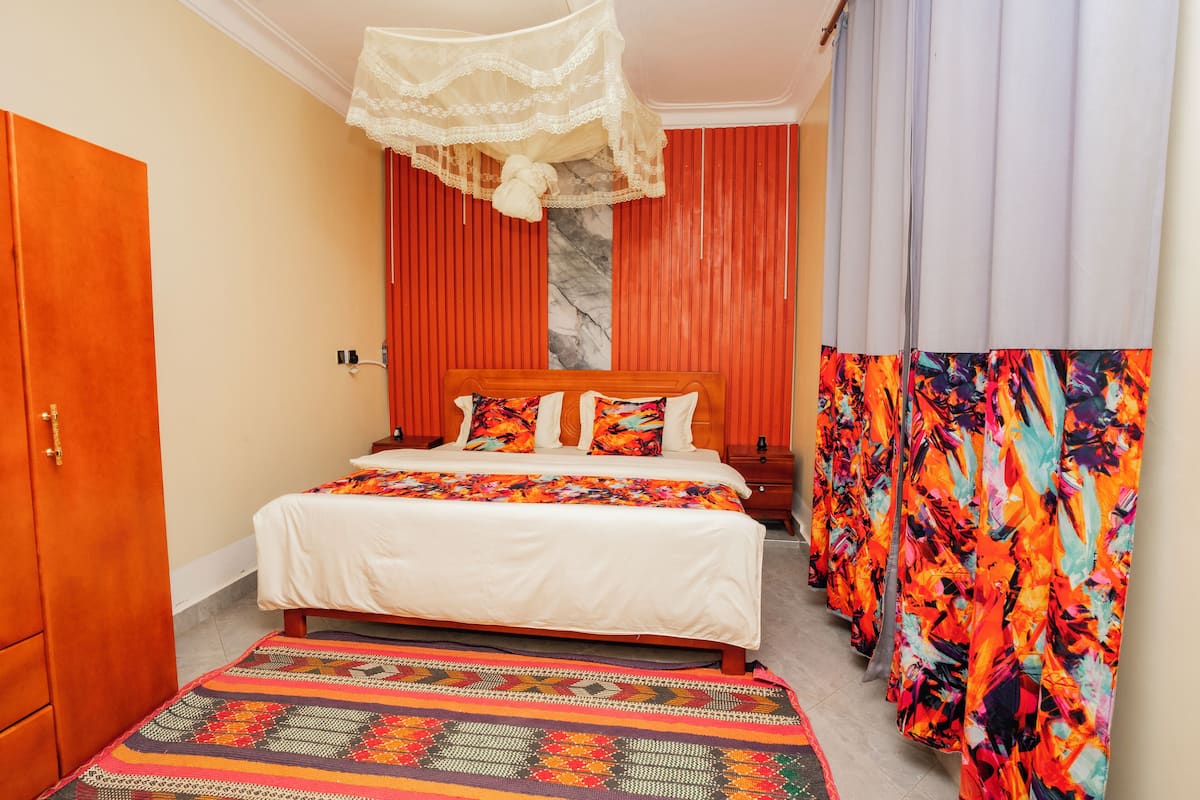 Un dormitorio con cama, armario, mesita de noche, alfombra estampada y cortina con diseño floral.