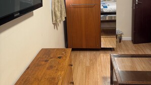 Une chambre avec un bureau en bois, une télévision, une armoire et un lit muni d’un rideau.