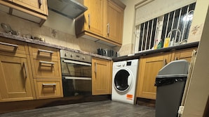 Une cuisine dotée de meubles en bois, d’une hotte de cuisson en acier inoxydable, d’un four encastré, d’un lave-linge et d’une poubelle.
