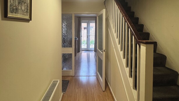 Un couloir doté d’un plancher en bois, un escalier avec une rampe et une porte donnant sur un espace extérieur.