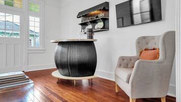 Une pièce avec un plancher en bois, une table ronde noire avec un plateau blanc, un fauteuil gris avec un coussin, une étagère murale ornée d’objets décoratifs et un téléviseur à écran plat.