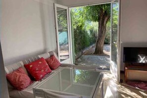 A room with a glass-enclosed hot tub, a sofa with red cushions, and a television on a wooden stand. - Cozy maisonette (F1), rated 3*—100 m from the sea and beach (Hyères)