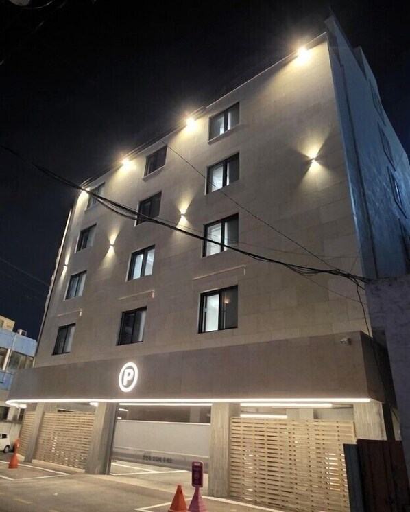 Un edificio de varios pisos con acceso a un estacionamiento, iluminado por luces superiores.
