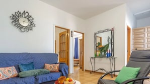 A living room with a blue sofa, a black chair, a small table with a tray of snacks, and a decorative wall clock. - "El pajal House Relax" by Interhome (Santa Ursula)