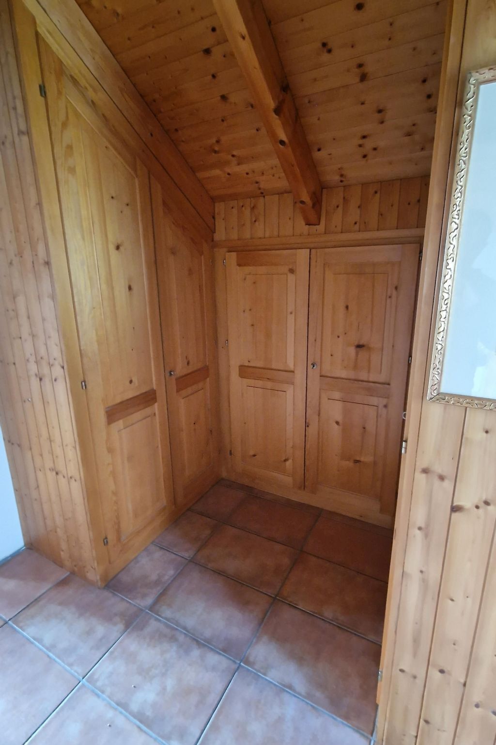 A wooden room with a tiled floor, wooden walls, and a ceiling with exposed beams.