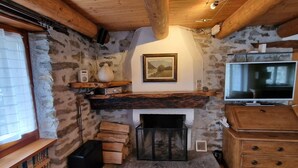 A rustic room with a stone wall, wooden beams, a fireplace, a television, and a bookshelf.