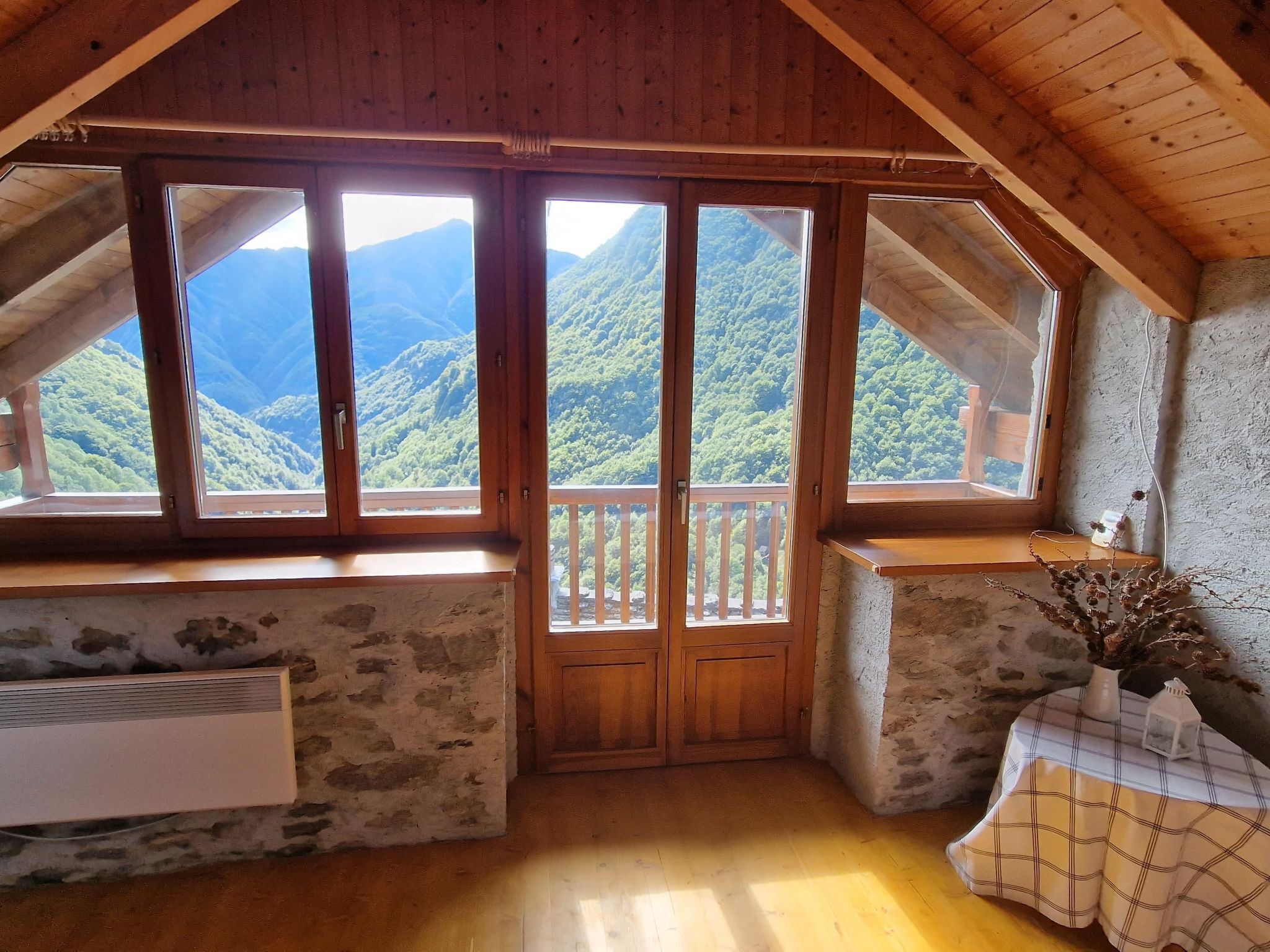 A rustic room with wooden beams, a balcony, and a view of green mountains.