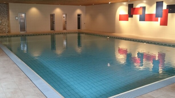 Una piscina interna con pareti piastrellate e soffitto in legno.