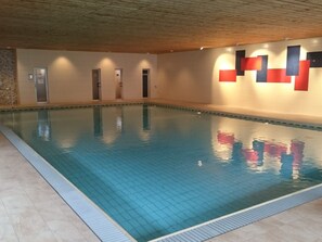 Ein Innenpool mit gefliesten Wänden und einer Holzbalkendecke.