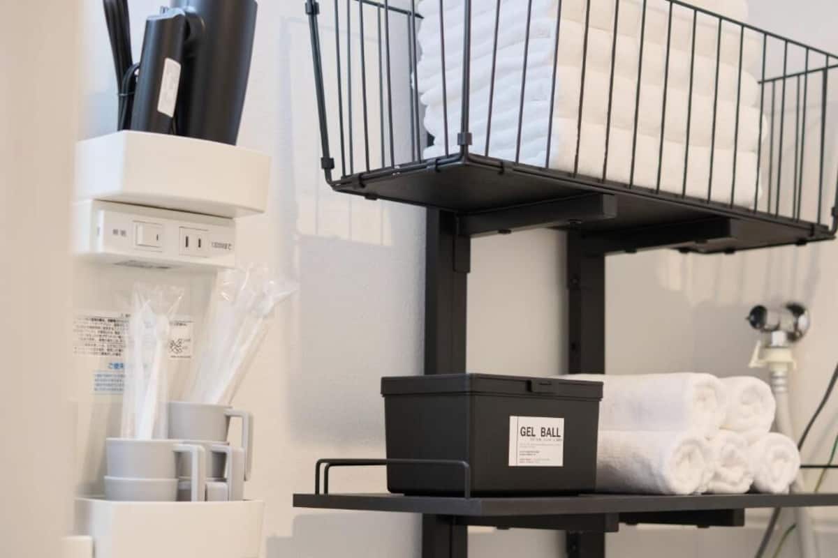 A bathroom with a black shelf holding a black box labeled "GEL BALL" and a towel rack with rolled towels.