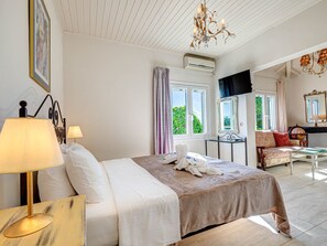 A hotel room with a bed, bedside lamps, a chandelier, a window with curtains, a small table, a sofa, and a mirror. - "Villa Nafsika" by Interhome (Kalami)