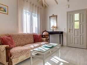 A living room with a patterned sofa, a glass-top coffee table, a globe, and a piano. - "Villa Nafsika" by Interhome (Kalami)