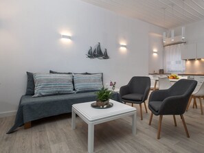 A modern living room with a grey sofa, two armchairs, a white coffee table, and a kitchen area in the background. - Studio mit atemberaubendem Blick auf das Meer by Interhome (Kalami)