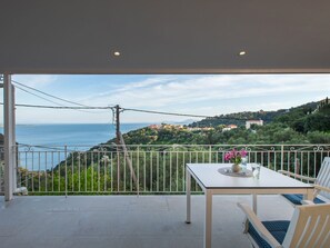 A balcony with a table and chairs, overlooking a coastal landscape with houses and greenery. - Studio mit atemberaubendem Blick auf das Meer by Interhome (Kalami)