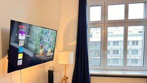 Habitación con televisión mostrando un perfil de Netflix, lámpara, radiador y ventana con cortinas.
