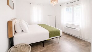 A bedroom with a bed, a standing heater, a wicker chair, and a window with curtains. - Miami Beach Escape Delightful 1 bdr Stay (Miami Beach)
