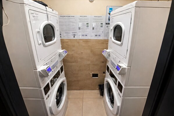 A laundry room with two stacked washing machines, a tiled wall with informational posters, and a drain in the floor. - Miami Beach Escape Delightful 1 bdr Stay (Miami Beach)