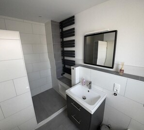 A modern bathroom with a shower, a sink, and a mirror. - Bungalow in Dornumersiel (Dornum)