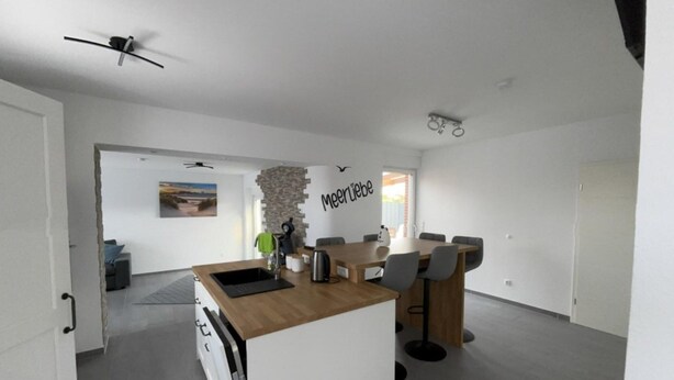 Une cuisine moderne avec un îlot en bois, un coin repas avec une table et des chaises, et un espace de vie avec un canapé et un tableau.