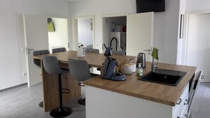 Une cuisine moderne avec un plan de travail en bois, des tabourets de bar, une cuisinière encastrée et un téléviseur à écran plat fixé au mur.