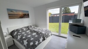 Une chambre à coucher comprenant un lit, une table de chevet, une commode et une porte-fenêtre coulissante donnant sur un jardin.