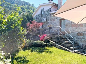 Un edificio de piedra con un balcón, un jardín con diversas plantas y un paraguas grande.