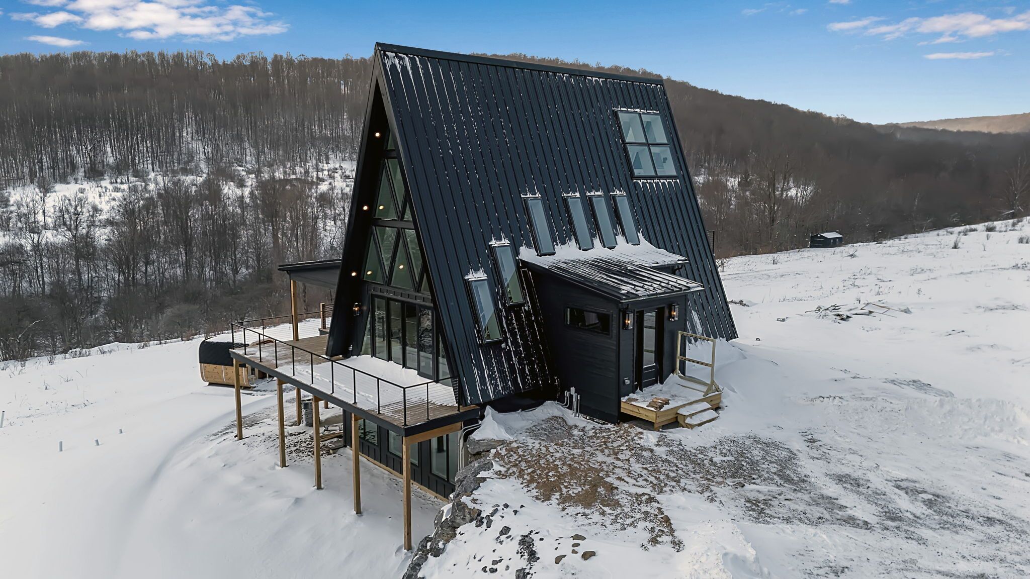 A modern, dark-colored cabin with a sloped roof, large windows, and a wooden deck.