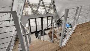 Een modern interieur met een houten trap die leidt naar een balkon met grote ramen, met uitzicht op een besneeuwd landschap.