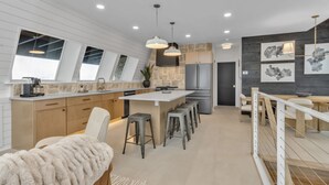 Een moderne keuken met een centraal eiland, hanglampen en een eetgedeelte met een hoge plafon en dakramen.