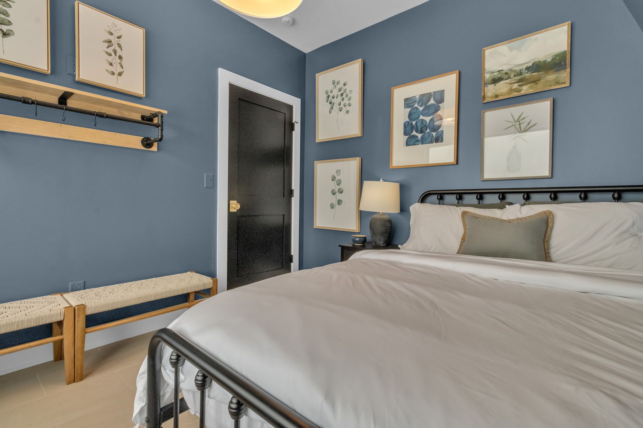 Un dormitorio con cama, banco, estante en la pared, puerta y cuadro enmarcado.