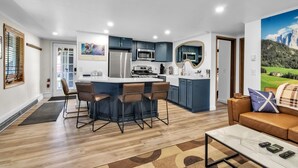 A modern kitchen with a central island, bar stools, and a dining area with a sofa and coffee table. - Cute Cottage1/2 mile to Village, Hot Tub (Ellicottville)