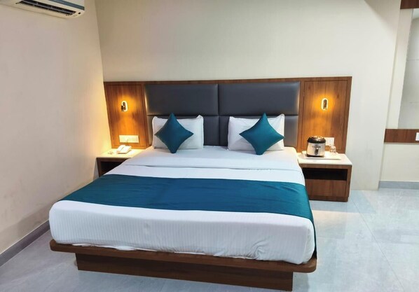 A hotel room with a large bed, two bedside tables, and a nightstand with a coffee maker. - Hotel Cidade De Diu (Diu)