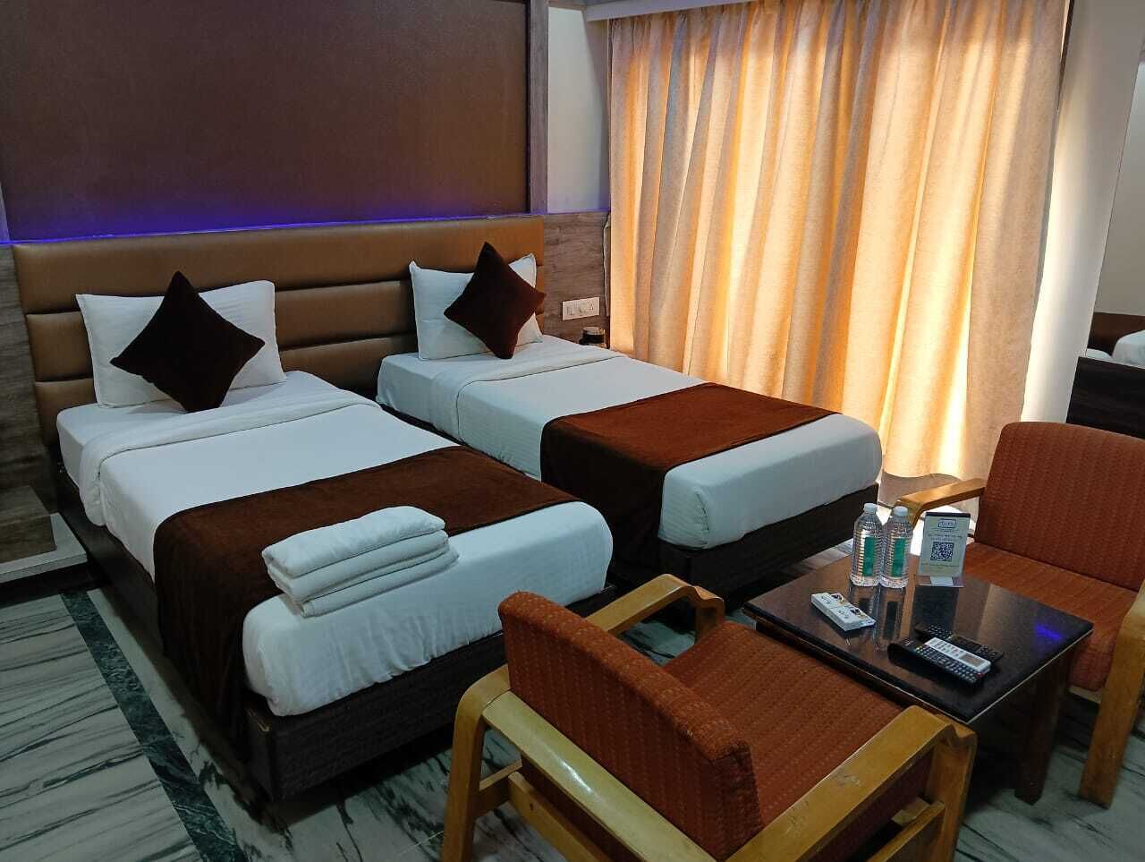 Une chambre d’hôtel avec deux lits, un petit canapé, une table basse et une fenêtre avec des rideaux.
