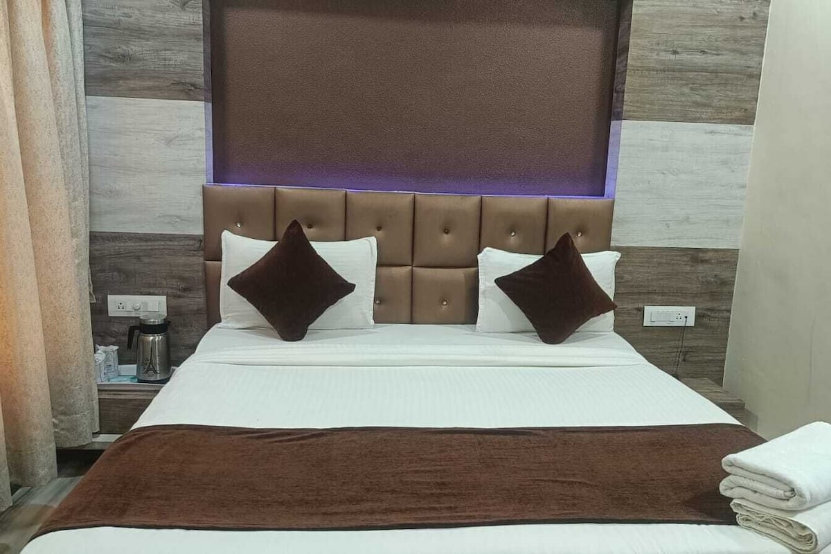 Una cama bien hecha con una manta marrón, dos almohadas y un cabecero con una lámpara.