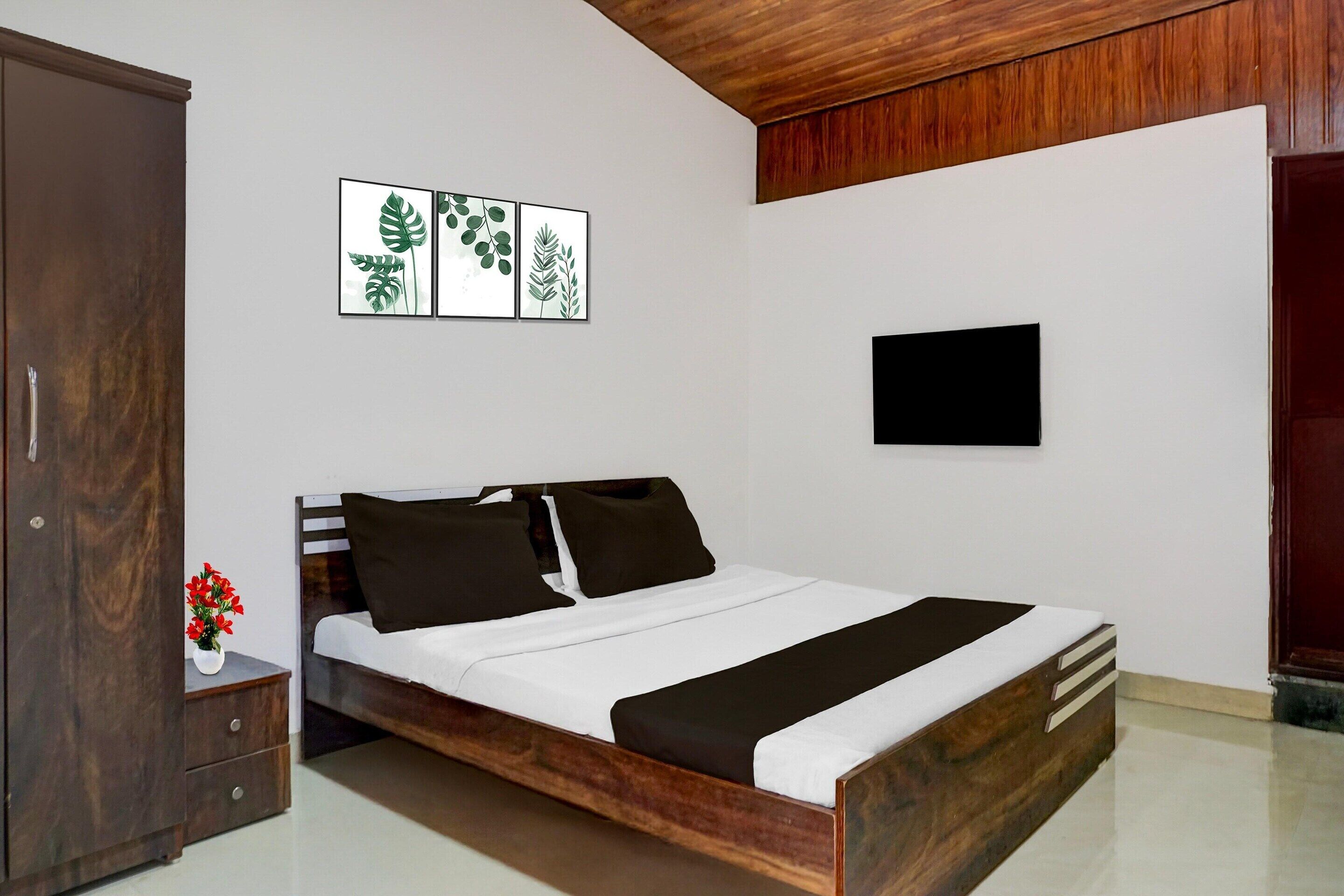A bedroom with a wooden bed, a nightstand with a vase of flowers, and a wall-mounted TV.