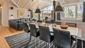 Un'elegante sala da pranzo moderna con soffitto alto, travi in legno e ampie finestre che offrono vista sul paesaggio esterno.