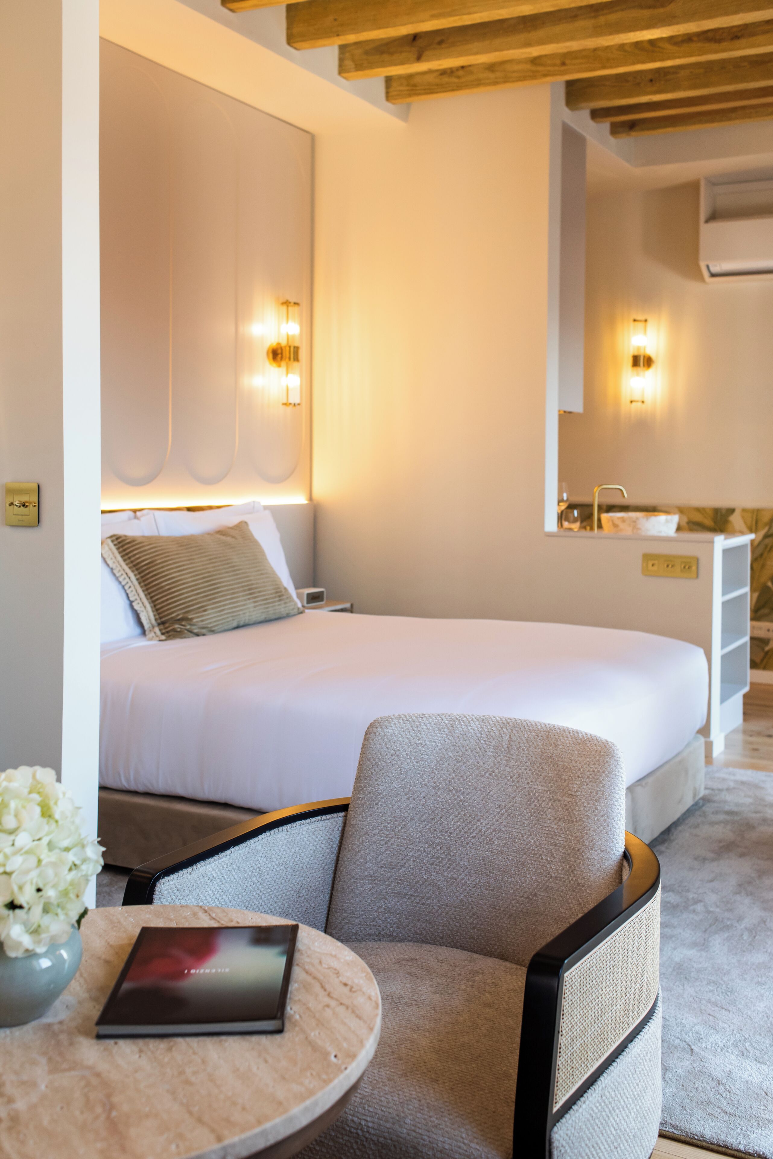 A bedroom with a bed, bedside table, chair, and a small table with a book.