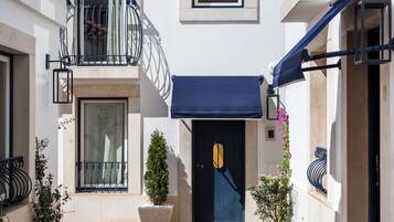 A building with a dark blue awning, a large potted plant, and a balcony with a metal railing.