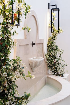 A stone water feature with a curved basin, a wall-mounted light fixture, and surrounding greenery. - Villa Dorothea (Lisbon)