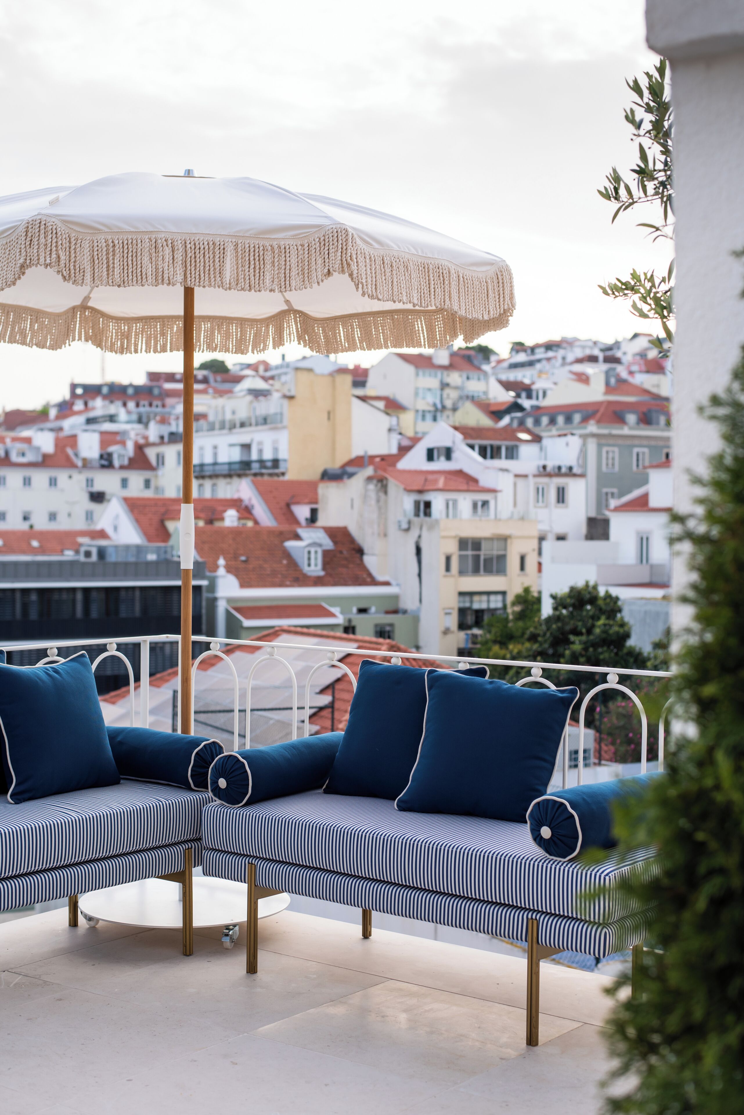 Uma varanda com um sofá listrado, um guarda-sol e vista para um horizonte urbano com edifícios de telhado vermelho.