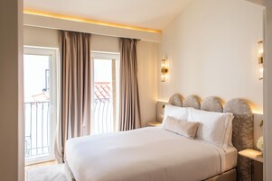 Quarto de hotel com uma cama grande, mesa de cabeceira, luminária na parede e vista para a varanda externa.