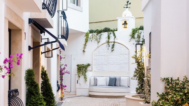 A narrow alleyway with a white sofa, greenery, and a decorative wall.