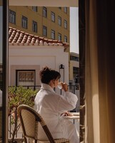 Uma pessoa sentada a uma mesa com vista para um edifício com várias janelas e telhado em telhas.