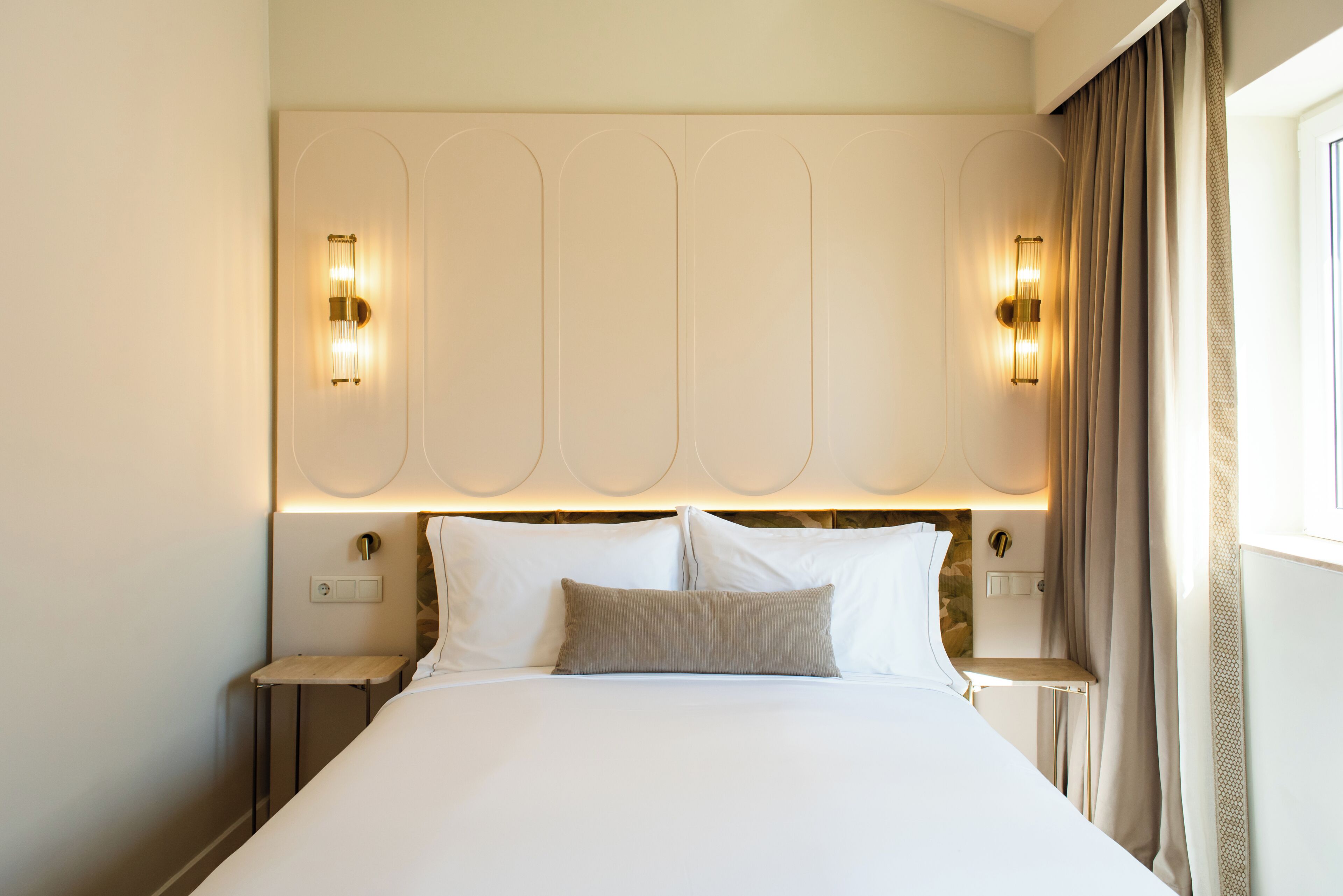 Ein Hotelzimmer mit einem großen Bett, zwei Nachttischen, einem Kopfteil mit integrierter Beleuchtung und einem Vorhangfenster.