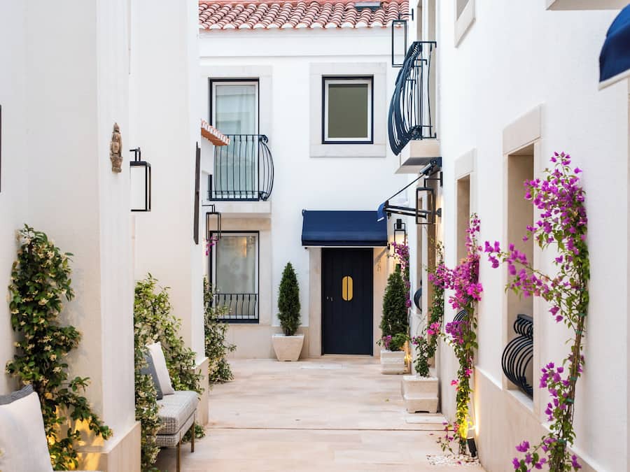 A narrow alleyway with a black door, white walls, and balconies with black railings.