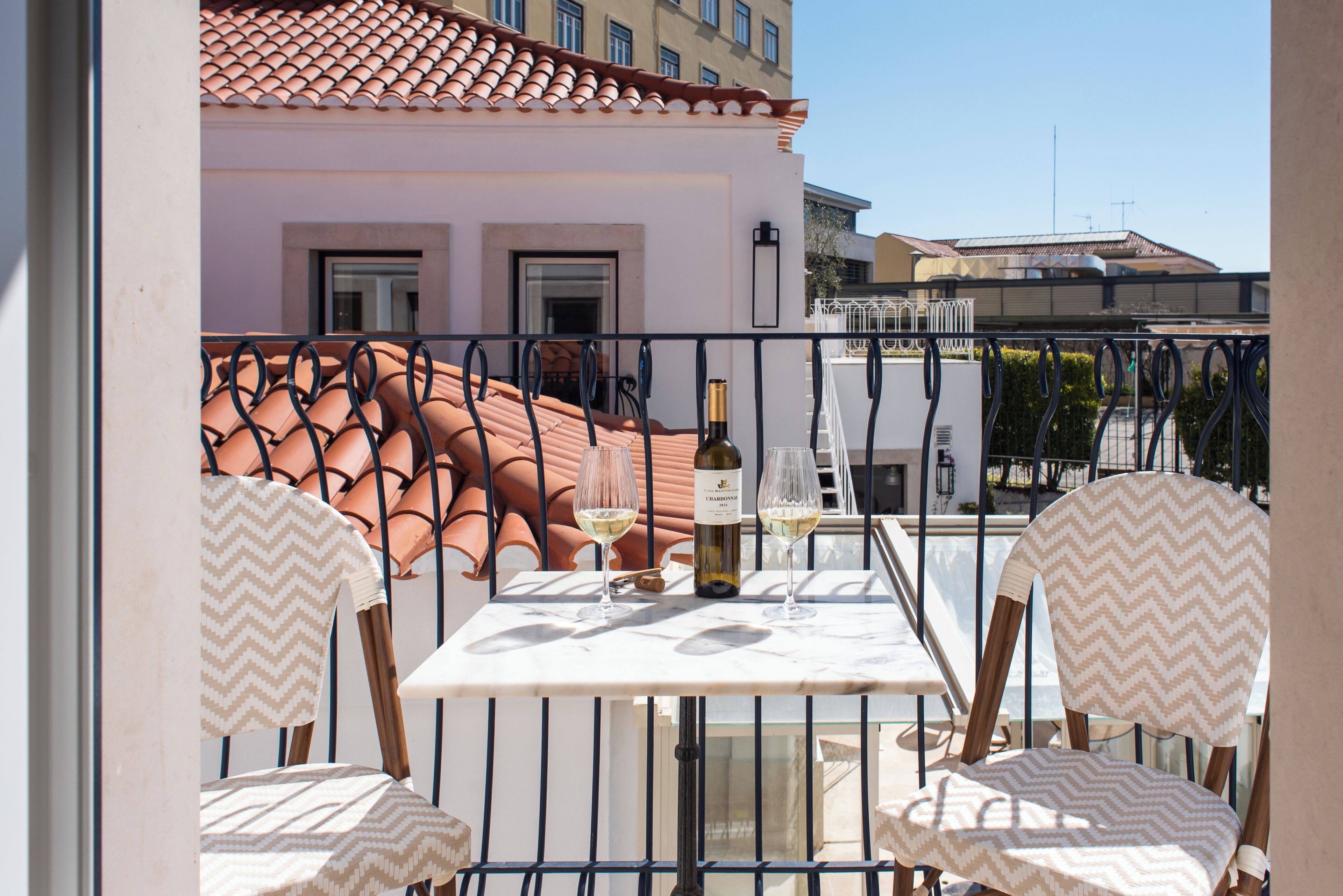 A balcony with a table and chairs, a bottle of wine, and a view of buildings.