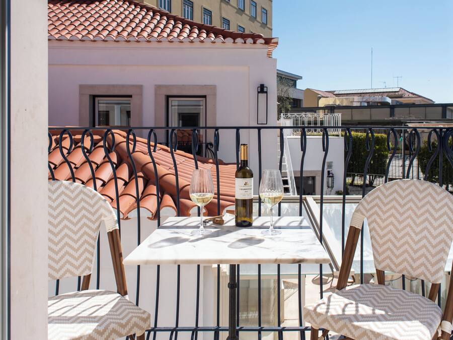 A balcony with a table and chairs, a bottle of wine, and a view of buildings.