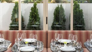A dining area with round tables, chairs, and a view of greenery and buildings.